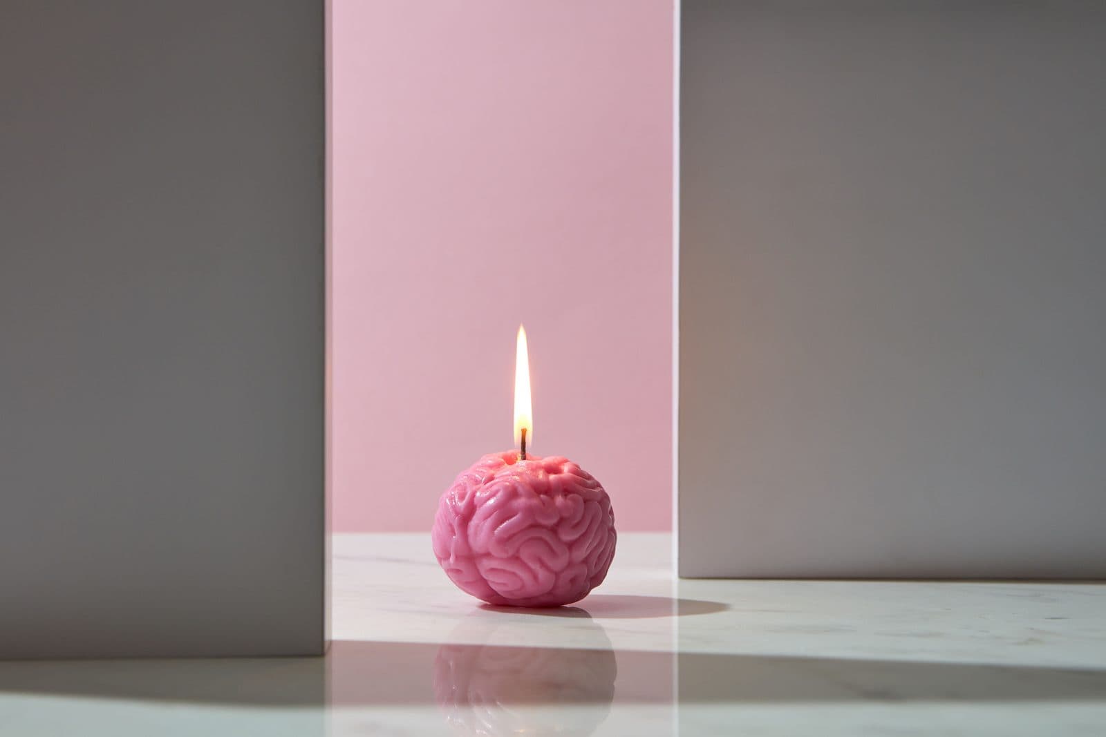 A pink brain candle with a steady flame on marble